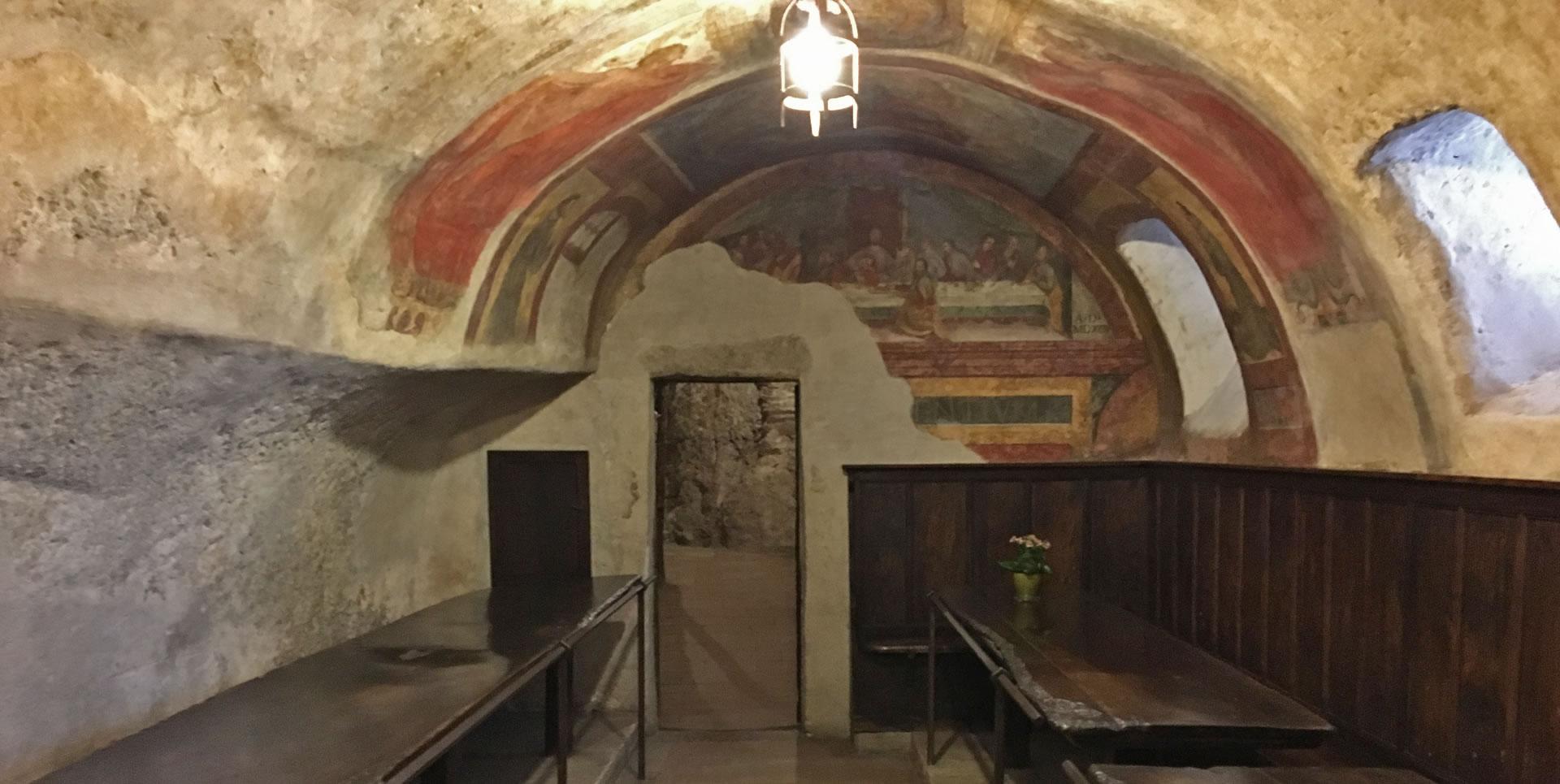 Refectory of the Eremo delle Carceri, carved into the rock, with ancient frescoes and simple wooden furnishings.