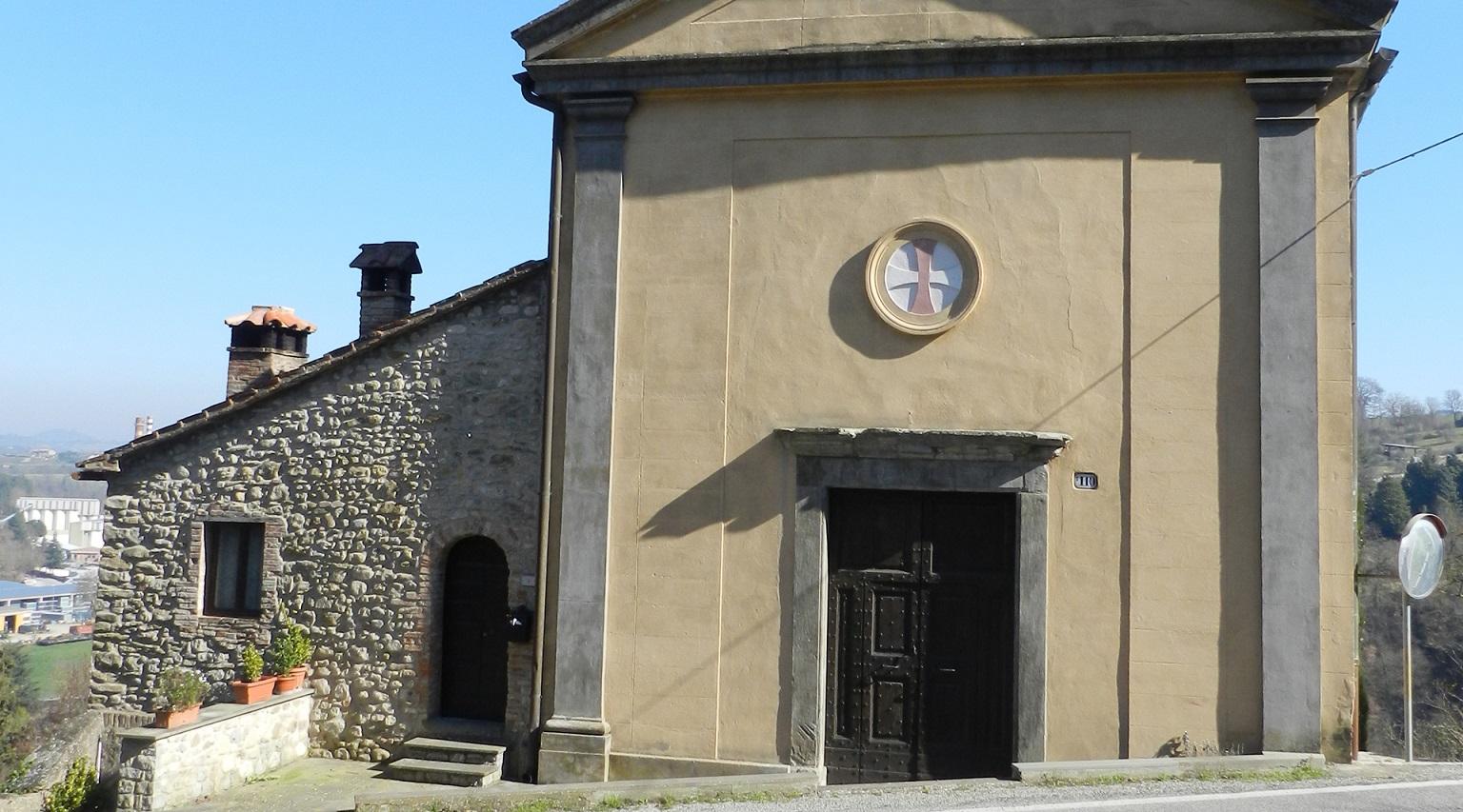 Facciata di una chiesa con porta in legno sormontata da un piccolo rosone centrale con stemma con croce greca.