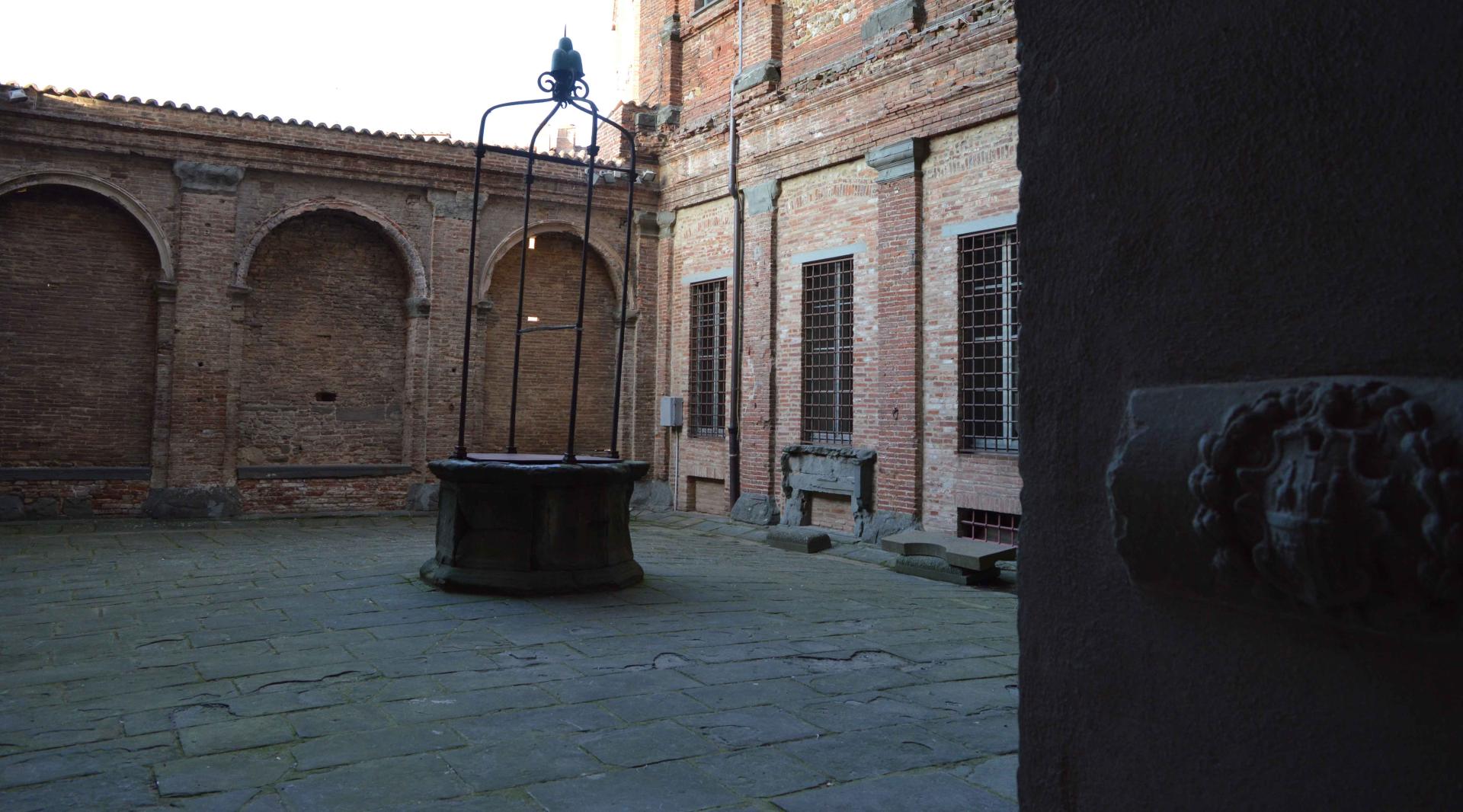 The inner courtyard of the palace, with an ancient stone well in the center. The ground floor windows overlook the courtyard, creating an intimate and evocative atmosphere.