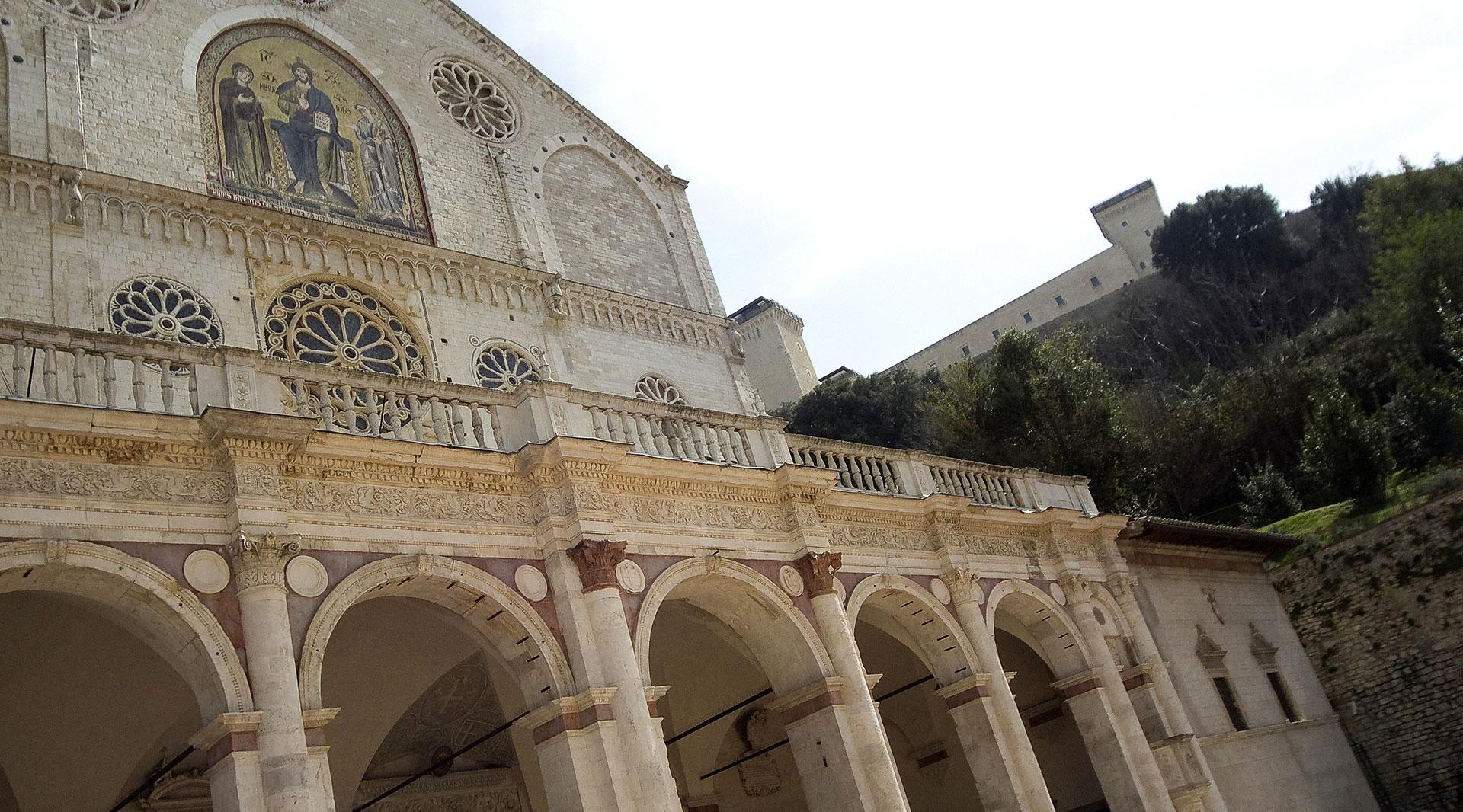 Façade de la cathédrale de Spolète avec portique à arcades, rosaces, mosaïque dorée et la Rocca Albornoziana en arrière-plan.