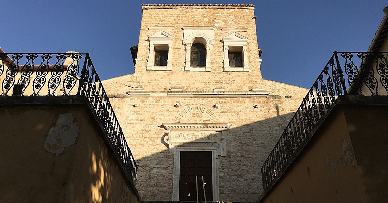 Facciata in pietra della basilica di San Salvatore con scalinata e balaustre in ferro, illuminata dalla luce del tramonto.