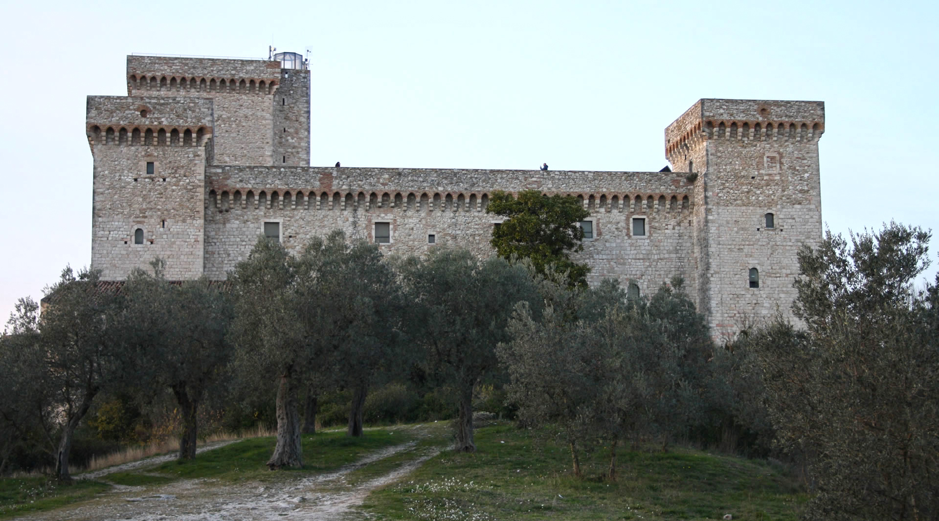 Front view of the Rocca of Narni, an imposing medieval stone fortress surrounded by olive trees