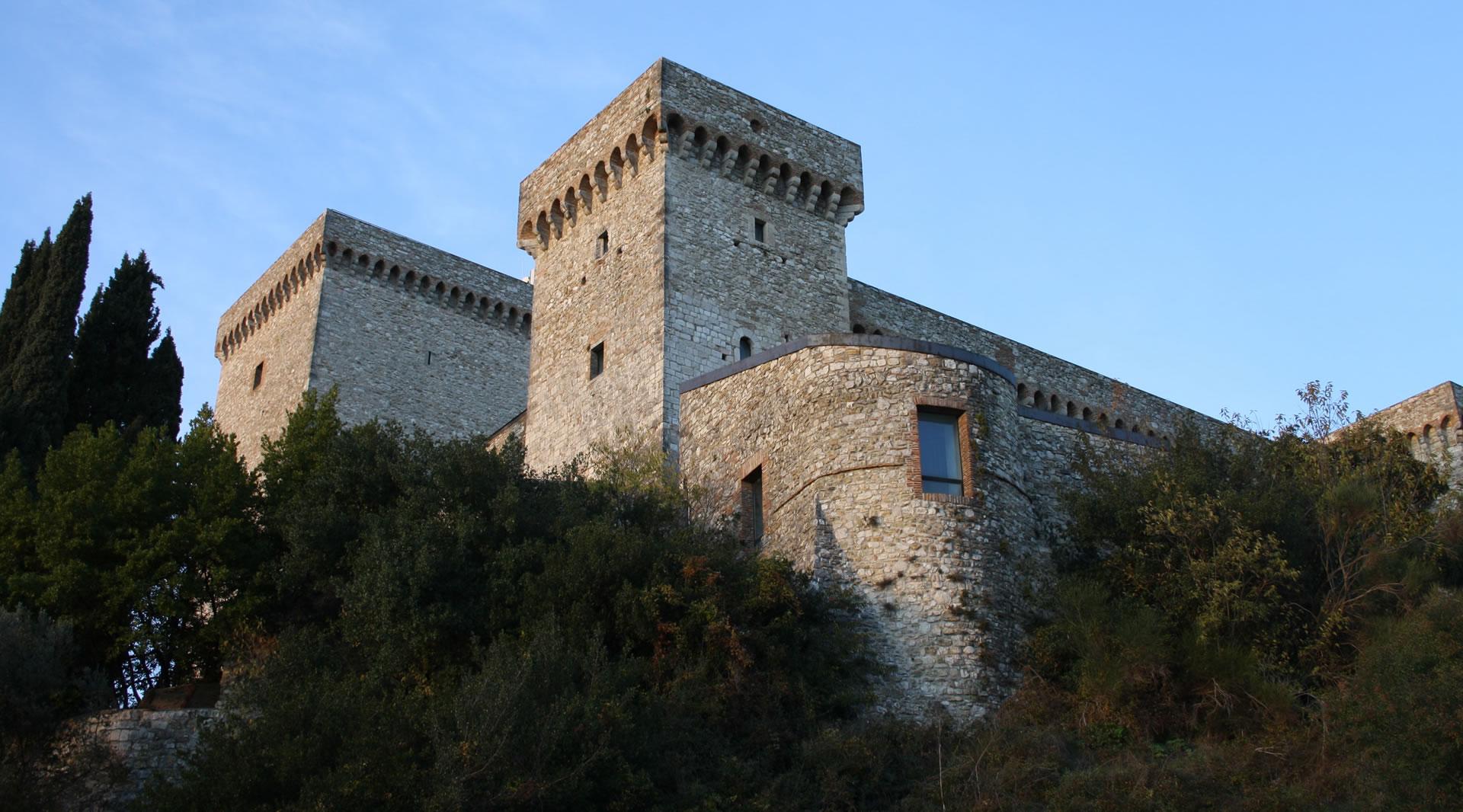 Vue latérale en contre-plongée de la forteresse de Narni, avec ses tours crénelées et ses murs de pierre émergeant de la végétation.
