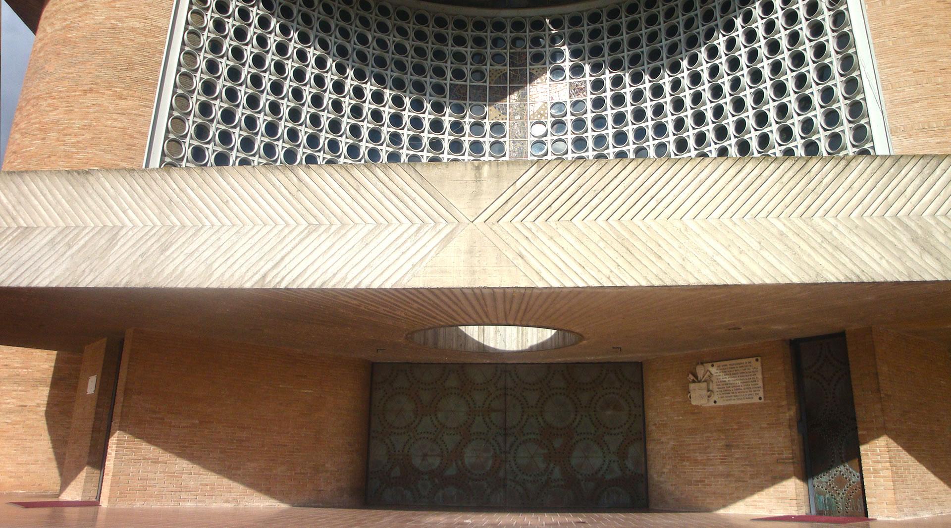 Portale in bronzo del Santuario di Collevalenza, con sovrastante parete traforata in vetro e cemento e dettagli geometrici.
