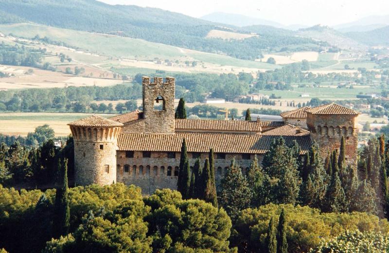 Medieval castle nestled in the green Umbrian hills, with battlemented towers and agricultural scenery in the background.