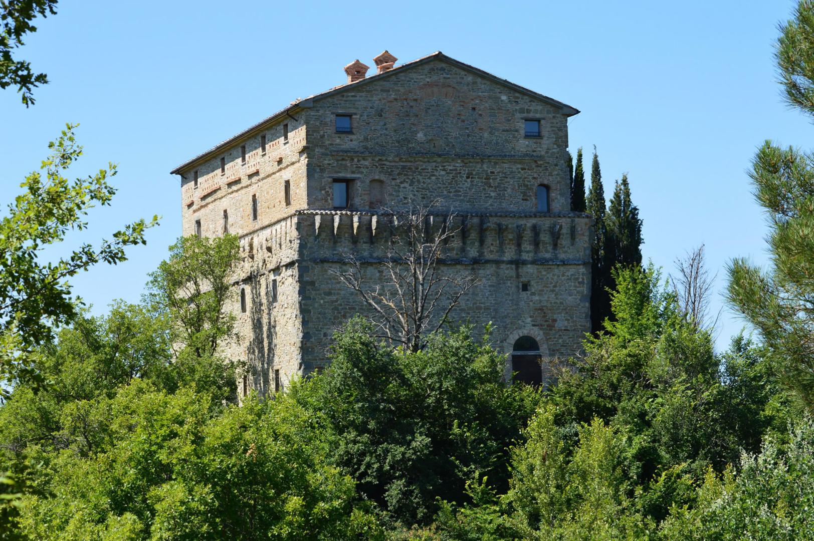 Die Rocca di Aries in Montone, imposantes Steingebäude, das aus dem Grün des Hügels unter heiterem Himmel hervorragt.