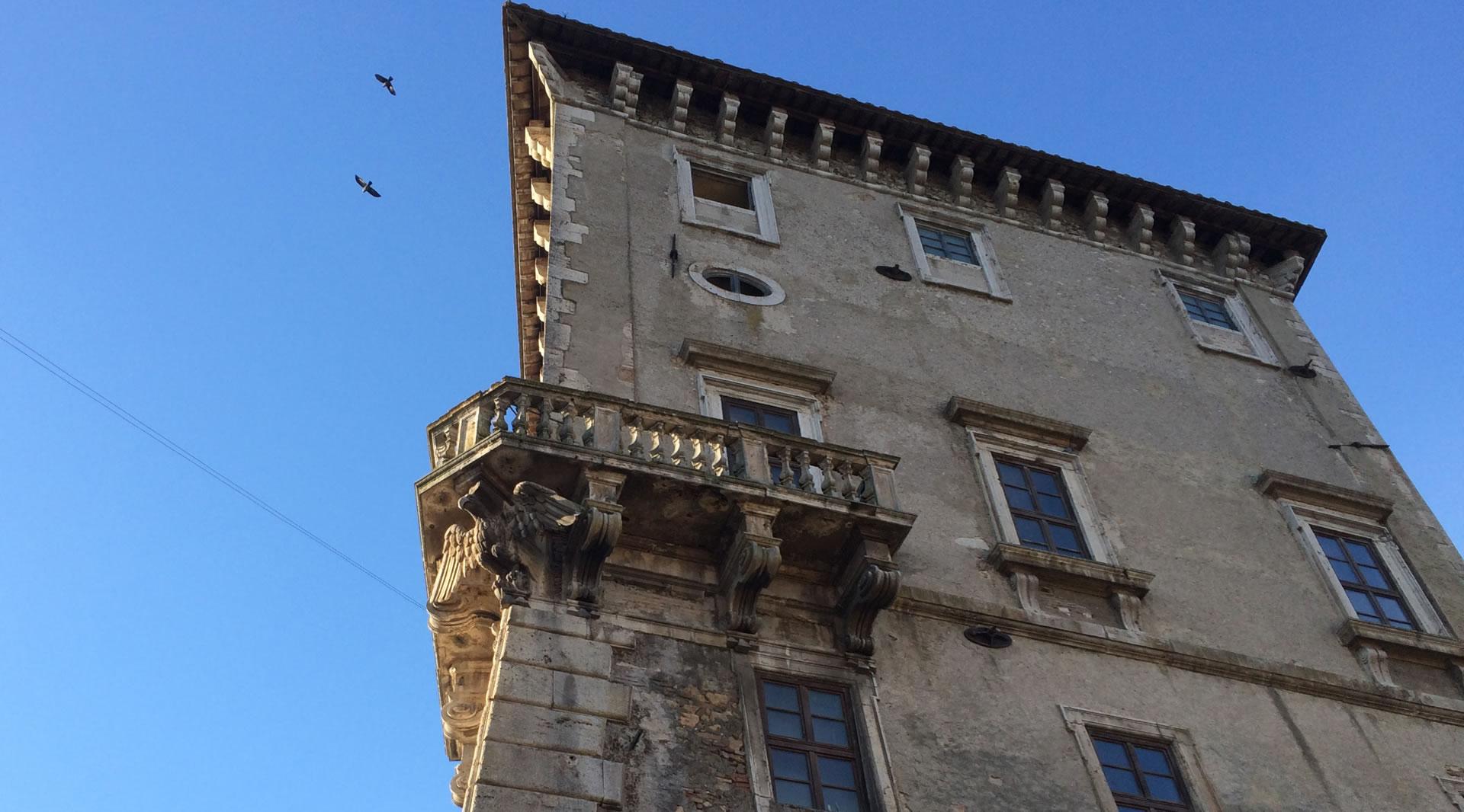 Il Castello di Giove visto dal basso, con un balcone in pietra e finestre storiche sotto un cielo azzurro.