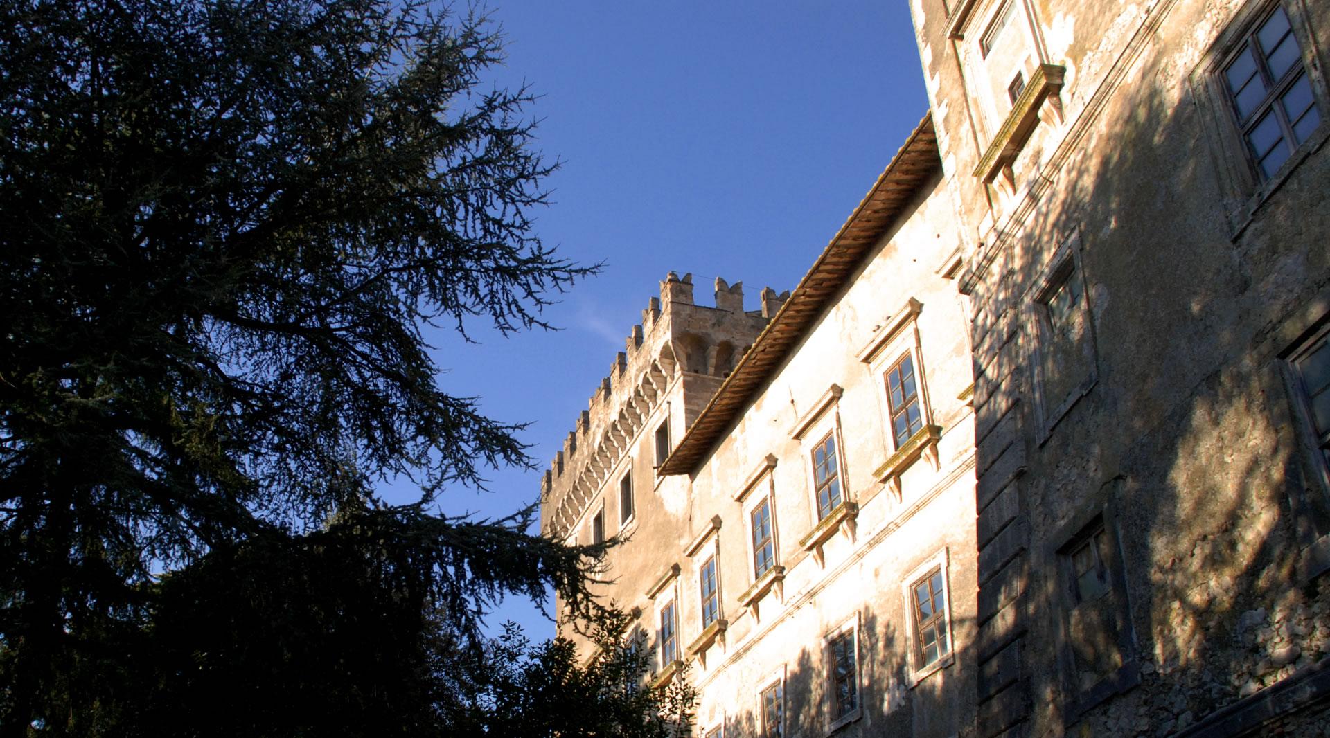 Facciata del Castello di Giove illuminata dal sole tra gli alberi, con una torre merlata sotto il cielo azzurro.