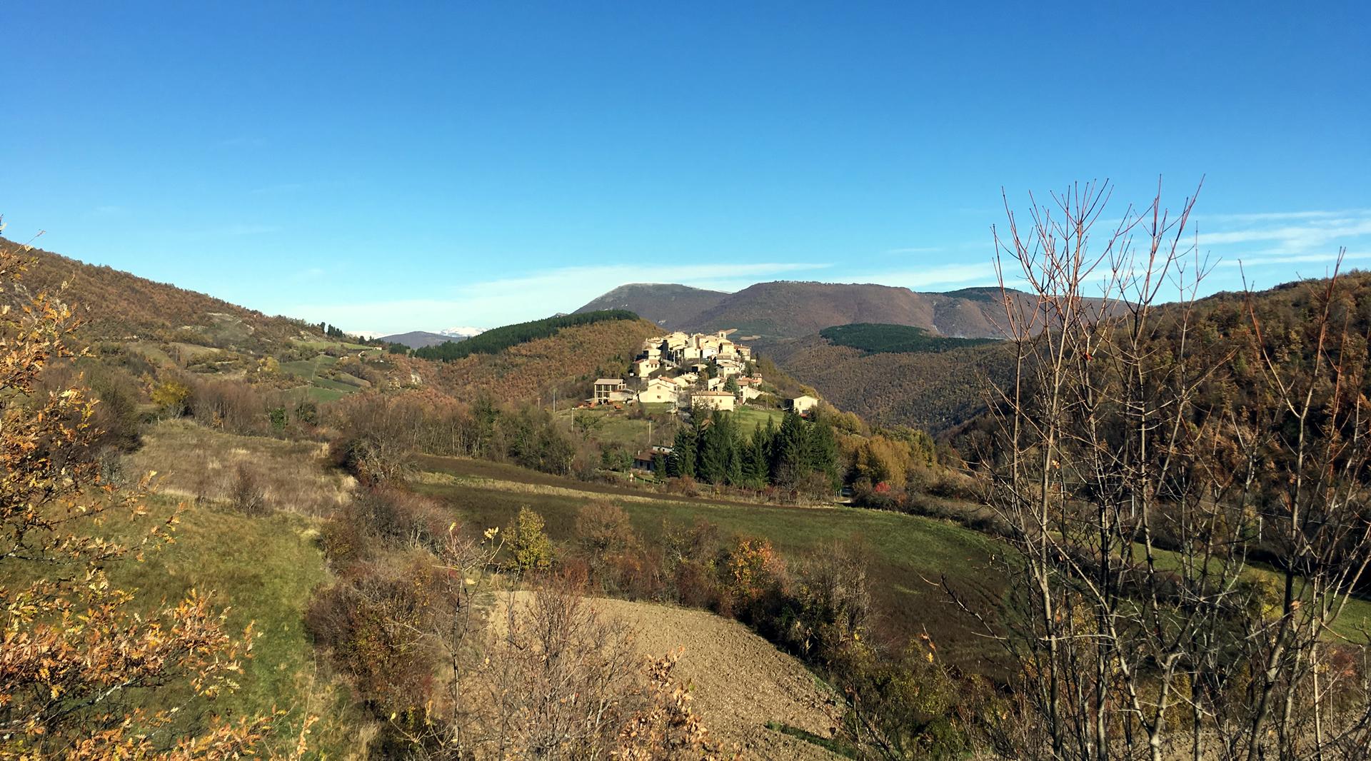 Vue du château d’Usigni perché sur une colline entourée de montagnes verdoyantes, avec un feuillage automnal et un ciel limpide.