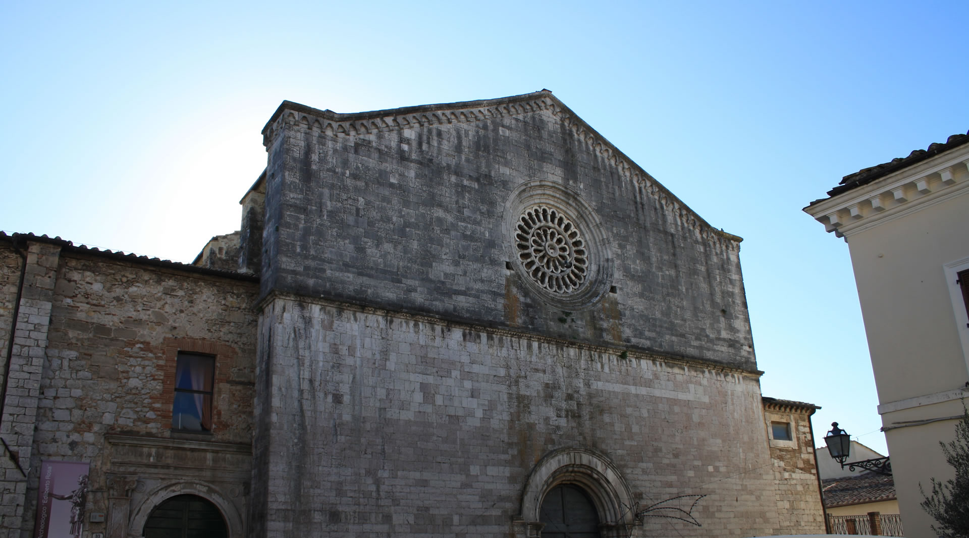 Facciata della chiesa di San Francesco ad Amelia con rosone centrale e un portale in pietra sotto un cielo limpido.