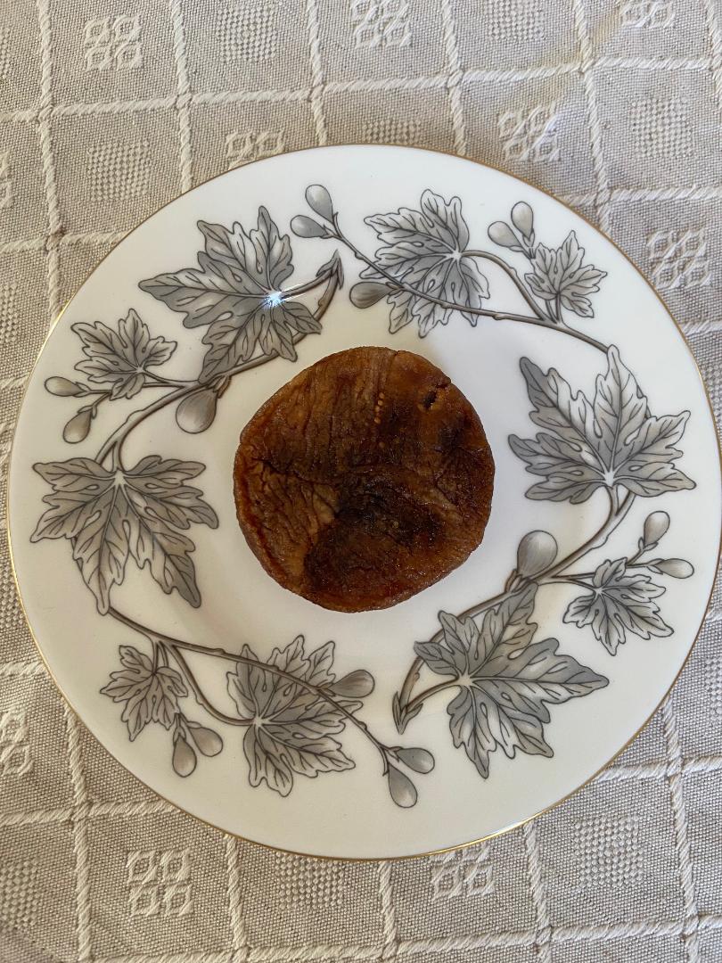 A stuffed dried fig on a porcelain plate decorated with grey fig leaves and a gold rim.