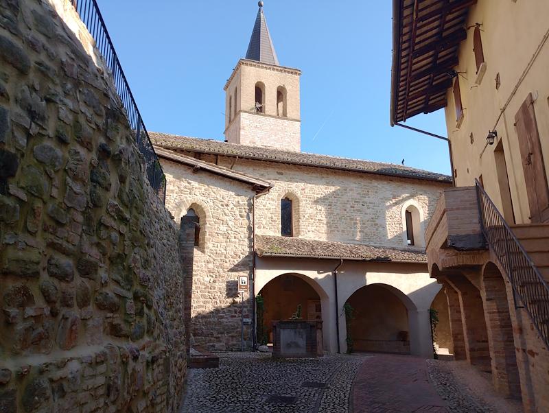 Ruelle pavée avec un puits devant l’entrée à portique de l’église de Santa Marina, avec le clocher en arrière-plan