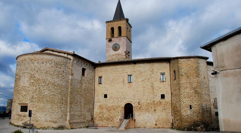 Stone church with apse, bell tower and clock, with a cloudy sky in the background