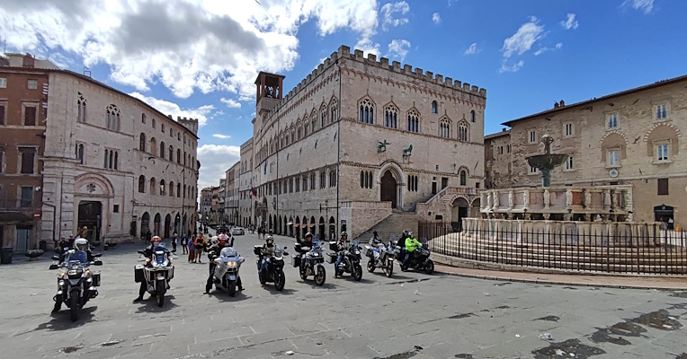 Motorcyclists lined up in Piazza IV Novembre in Perugia, with the Fontana Maggiore and the Palazzo dei Priori in the background.