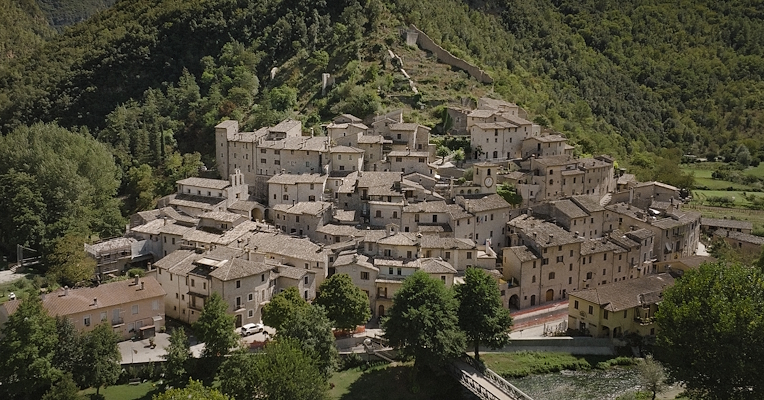 Aerial view of Scheggino, with stone houses and a medieval defensive wall, nestled in the green Valnerina valley.