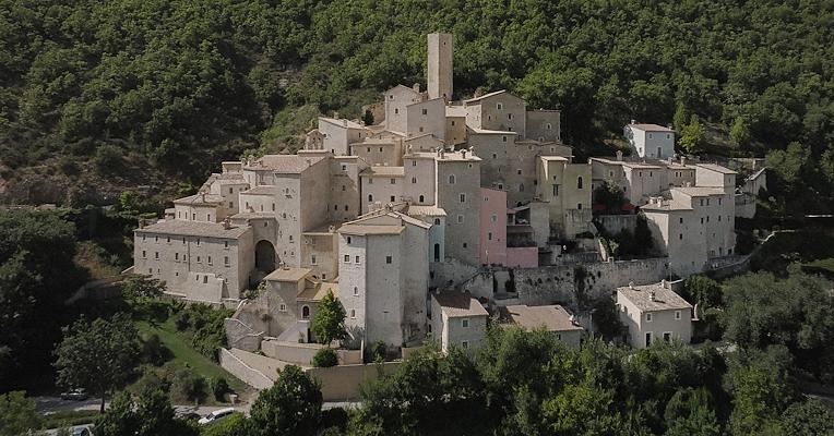 Luftaufnahme der Burg von Postignano, einem Ortsteil von Sellano, mit Steinhäusern, die sich an die umbrischen Wälder schmiegen.