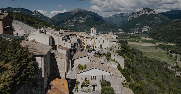 Aerial view of Montefranco, a perched Umbrian village with central church, stone roofs and green mountains in the background.