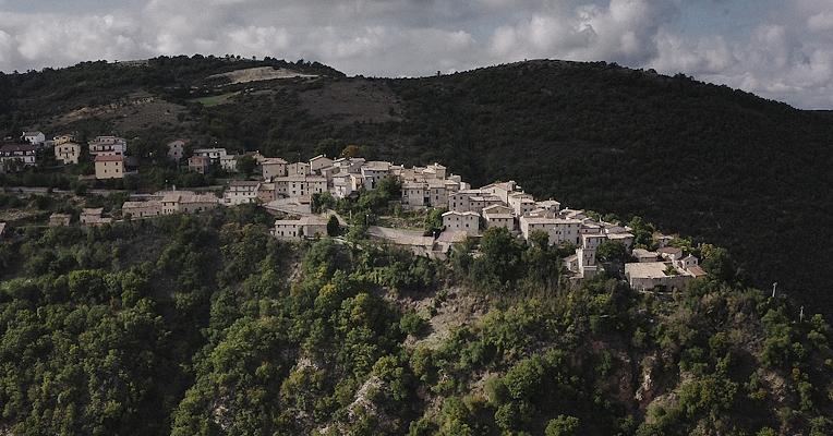Die mittelalterliche Schlossanlage von Poggiodomo auf einem Felsvorsprung, umgeben von unberührter Natur und grünen Wäldern