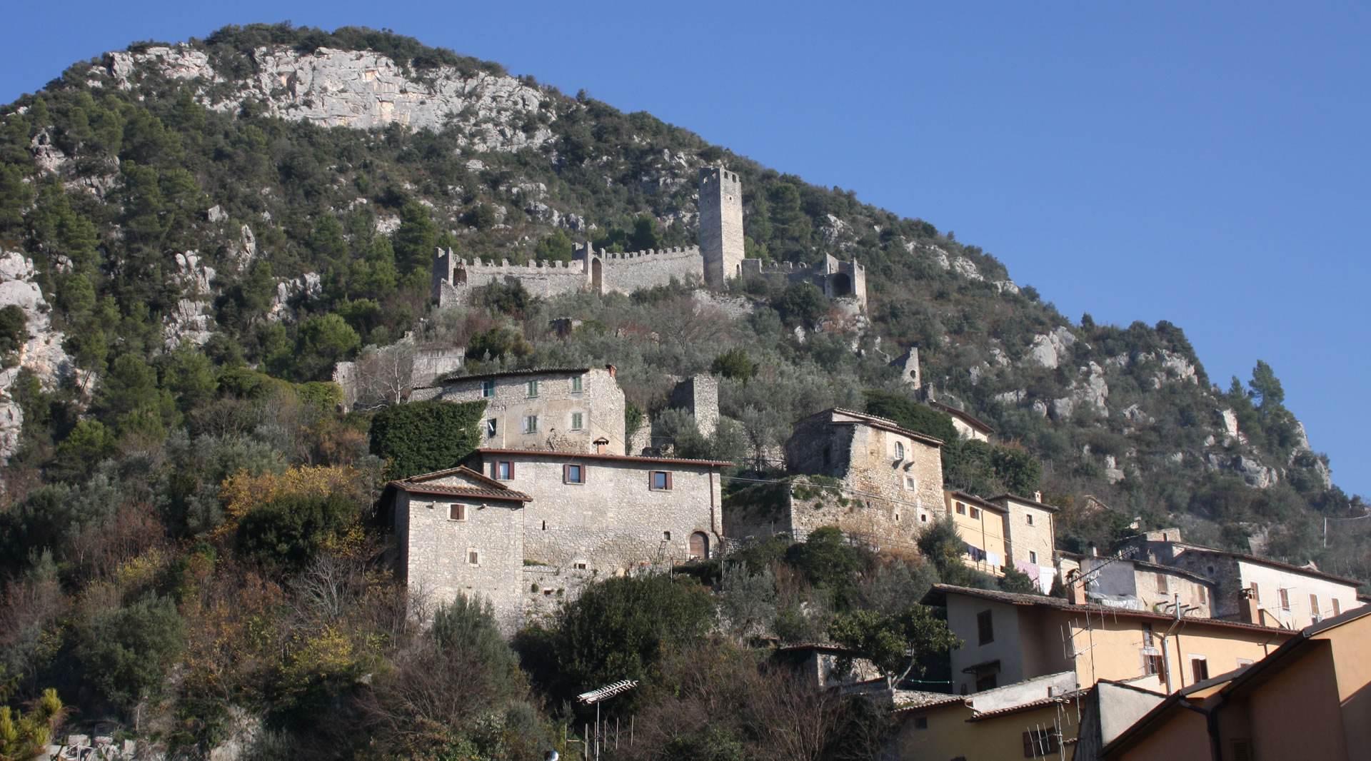 Medieval village of Ferentillo perched on the mountain, with stone houses and a fortified castle amid lush vegetation.
