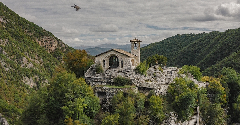 View of the Sanctuary of Roccaporena, nestled among Umbrian mountains, with a stone path rising through the vegetation.