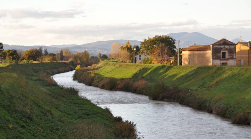 Fluss, der zwischen den grünen Ufern von Cannara fließt, mit Landhäusern und Hügeln im Licht des Sonnenuntergangs.