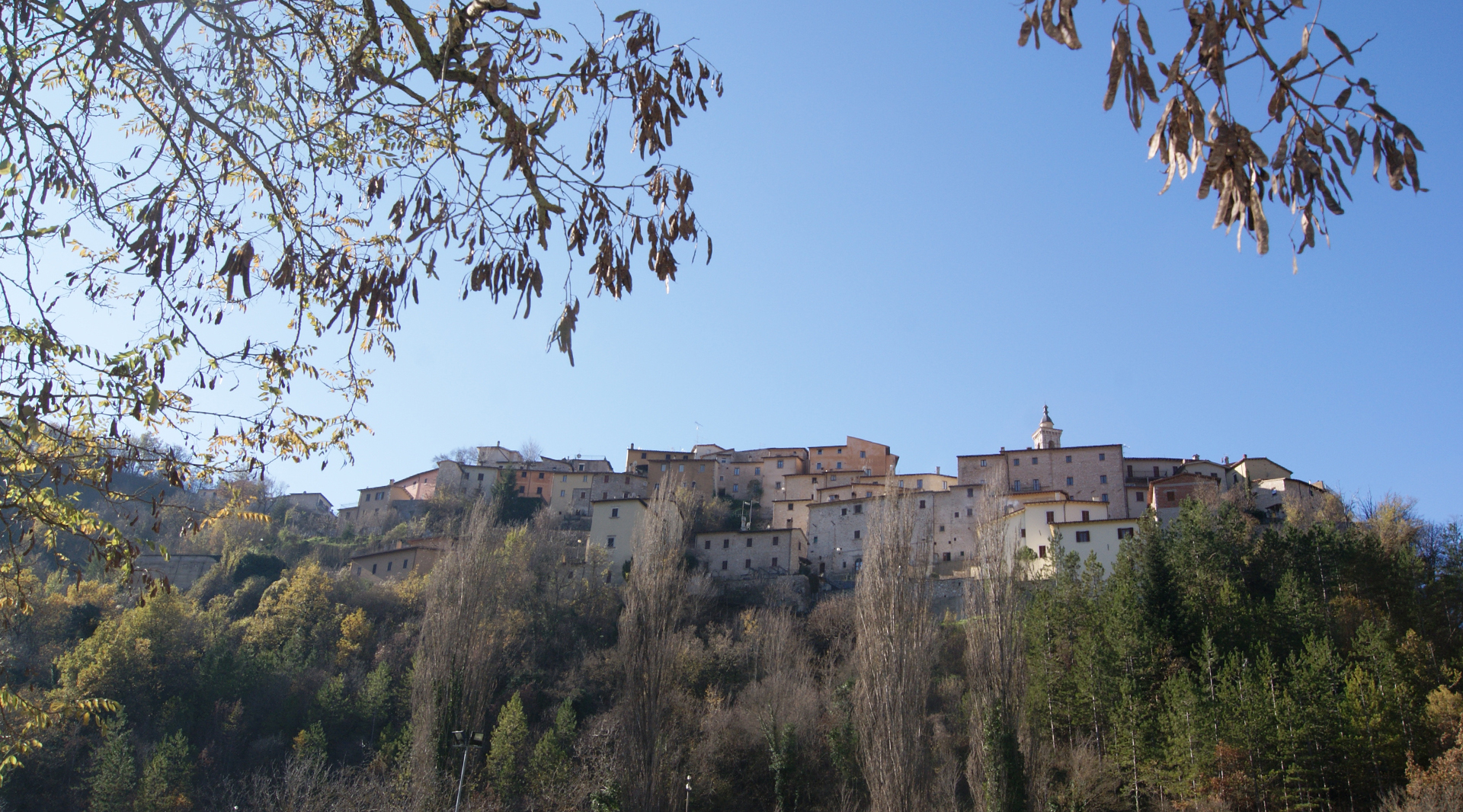 Panoramic view of the Umbrian village of Preci, perched on a slope and surrounded by woods, under a clear sky.