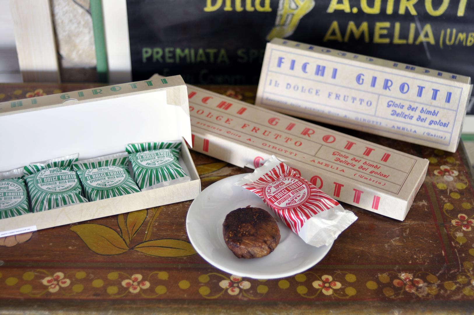 Packages of Fichi Girotti from Amelia, with figs wrapped in green and red paper and a fig served on a small white plate.