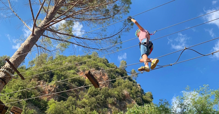 A person walks on a treetop adventure course wearing a safety harness