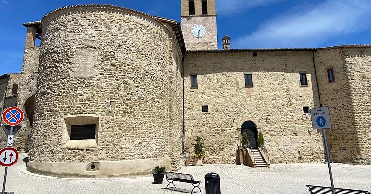 Tour circulaire en pierre de l’église de Santa Marina avec clocher, donnant sur une place avec un banc