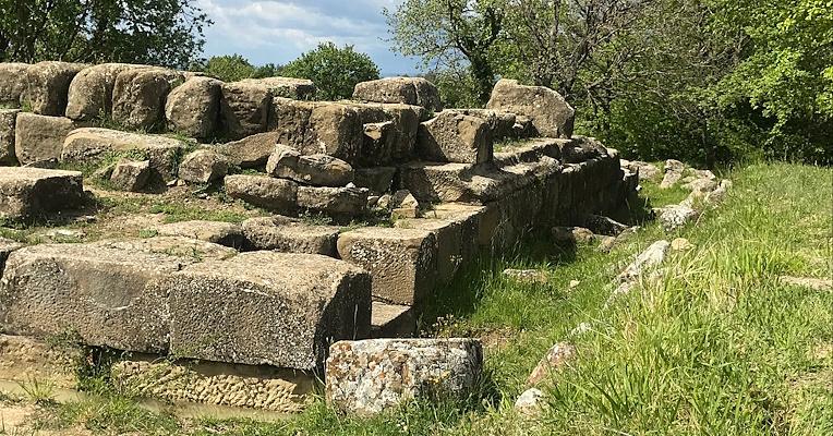 Remains of structures built with large stone blocks at the archaeological site of Urvinum Hortense, surrounded by vegetation.