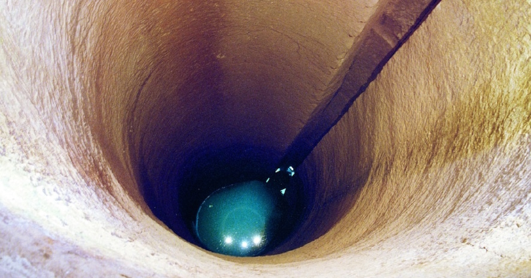 The cylindrical rock walls of the Pozzo della Cava with a rectangular shaft on the side.