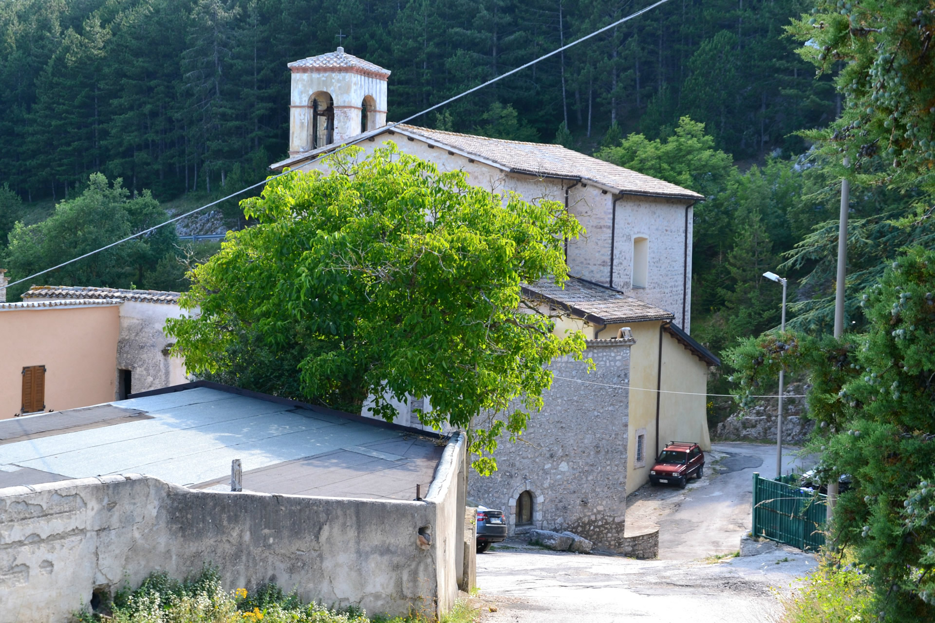Stone church of the Sanctuary of Cancelli with bell gable, surrounded by greenery on the edge of the village.