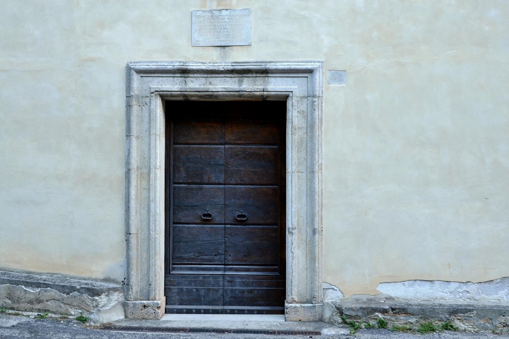 Stone portal with dark wooden door of the Sanctuary of Cancelli, set into the light plastered façade.