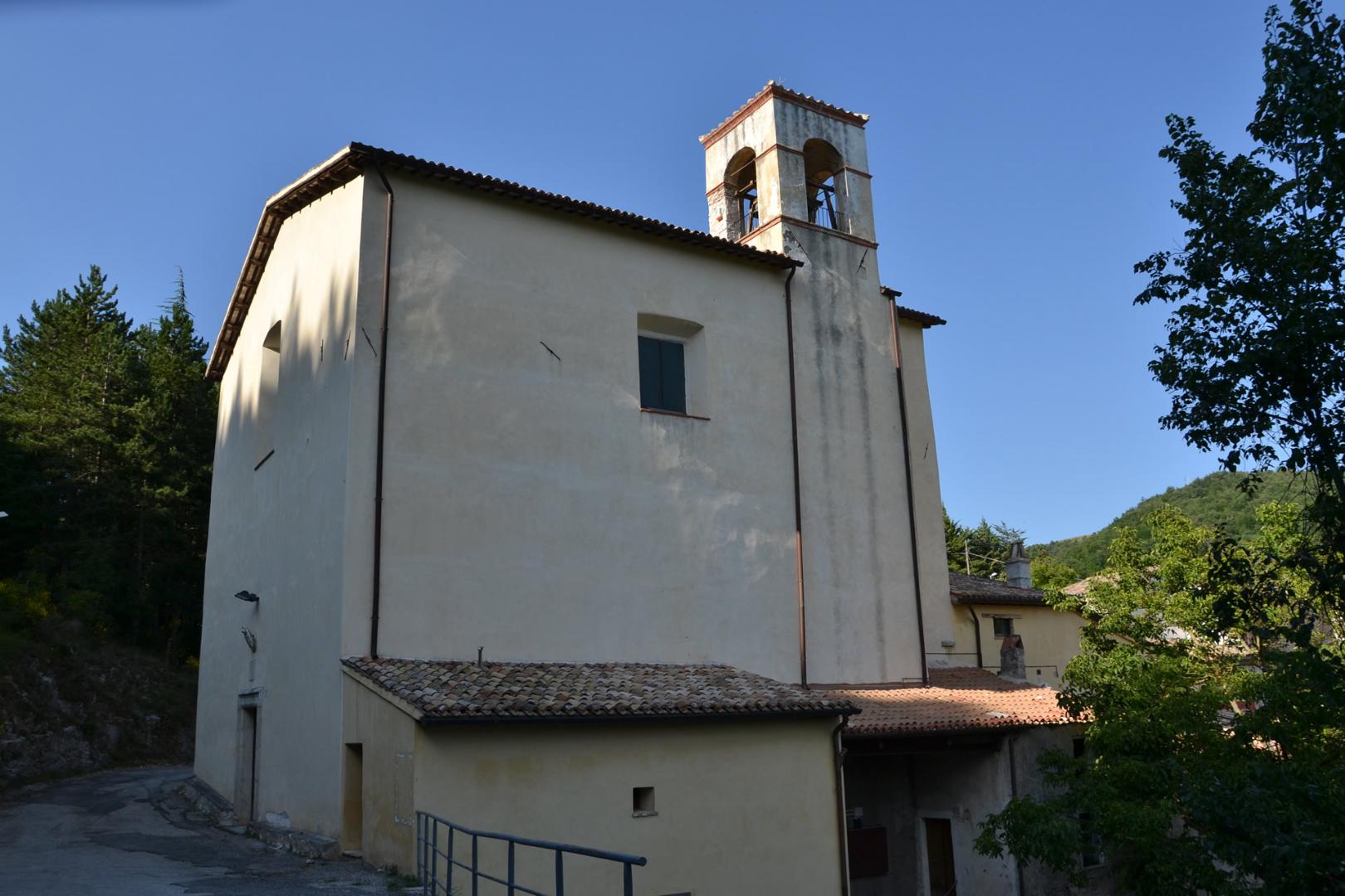 Side view of the Sanctuary of Cancelli with light plastered façade and bell gable against the blue sky.