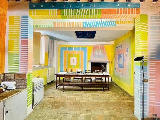 Dining room with colorful geometric wall patterns and a long wooden table in the center.