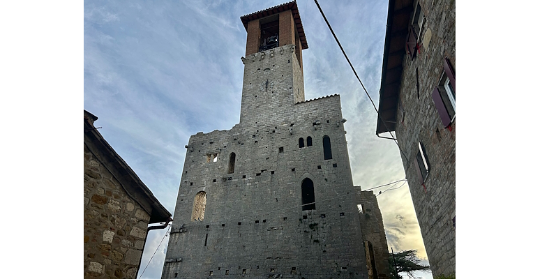 Façade frontale du château d’Agello, caractérisée par de vieilles fenêtres et dominée par un majestueux clocher surplombant l’édifice.