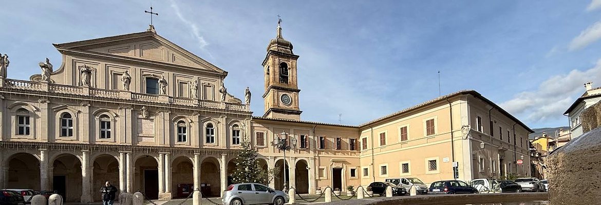 La facciata della Cattedrale di Santa Maria Assunta a Terni, con il suo portico colonnato e la torre campanaria laterale, con la fontana antistante che riflette il cielo e il palazzo adiacente la cattedrale