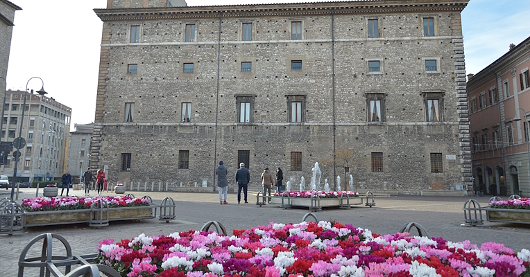 Piazza della Repubblica a Terni, con aiuole di ciclamini rosa, rossi e bianchi, mentre delle persone osservano Palazzo Spada