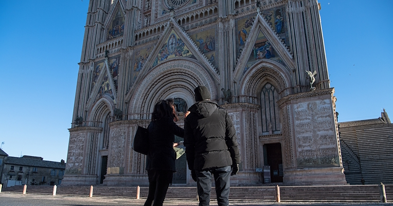 Due persone osservano la facciata del Duomo di Orvieto che si staglia contro un cielo limpido e sereno