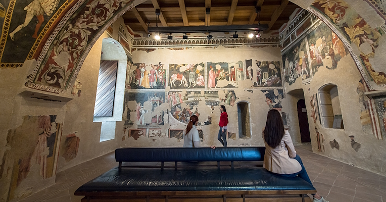 Interno della Camera Pinta della Rocca Albornoziana di Spoleto con visitatori che osservano le pareti decorate da affreschi