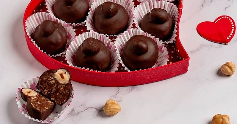 Scatola rossa a forma di cuore con all’interno otto cioccolatini, mentre fuori ci sono cuori rossi, nocciole e un cioccolatino a metà