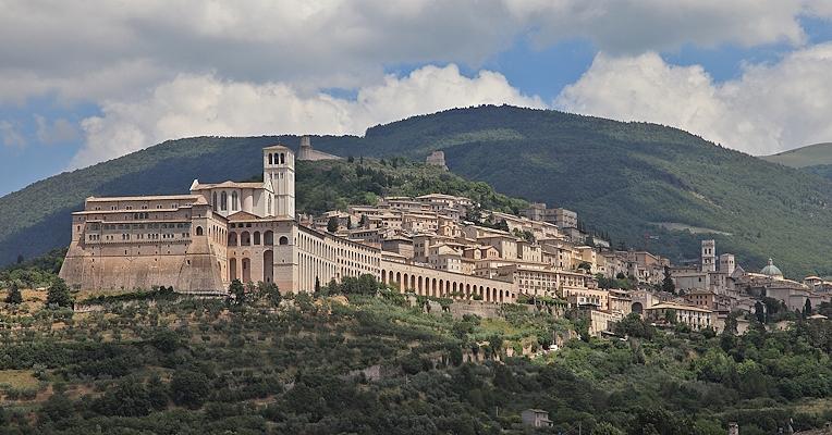 Panorama of Assisi from behind the Basilica, with the green hills of Mount Subasio in the background under a cloudy sky