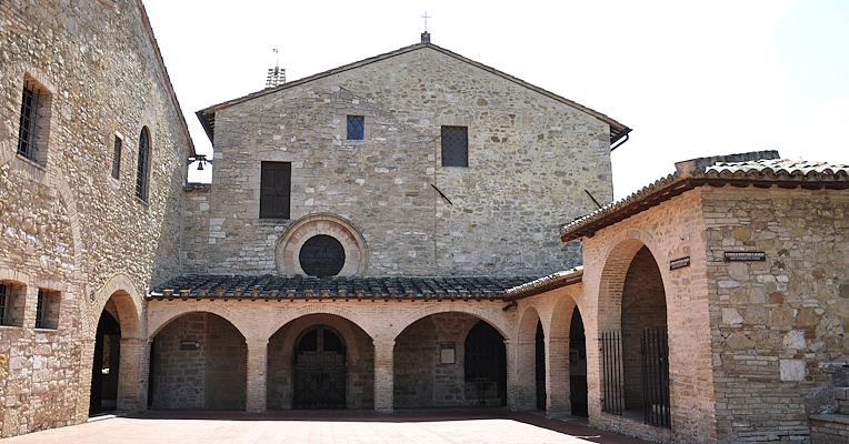 Outer square of the church of San Damiano in Assisi, featuring a stone courtyard, arches and a portico in medieval style.
