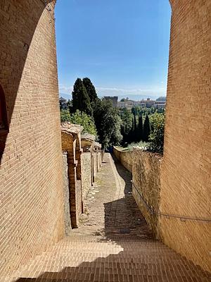 A brick staircase framed by historic walls, offering a panoramic view of trees, buildings, and hills under a clear sky.