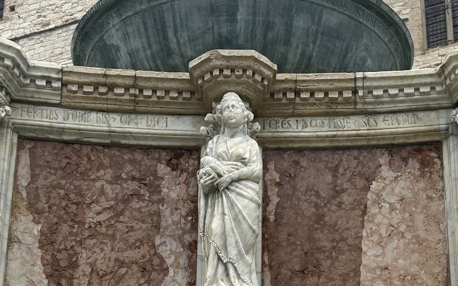 Sculpture de la Domina Lacii sur la Fontana Maggiore de Pérouse, tenant des vandoises dans la main, avec des inscriptions latines sur le marbre.