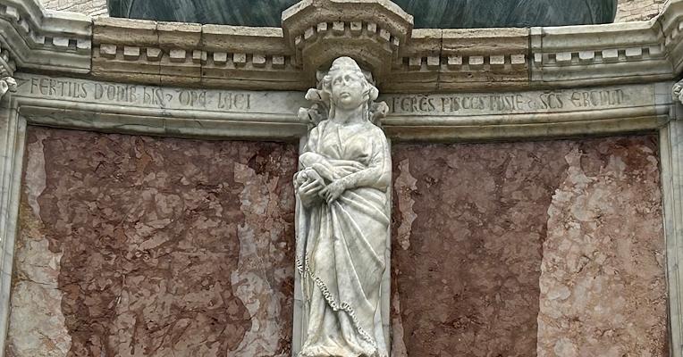 Sculpture de la Domina Lacii sur la Fontana Maggiore de Pérouse, tenant des vandoises dans la main, avec des inscriptions latines sur le marbre.