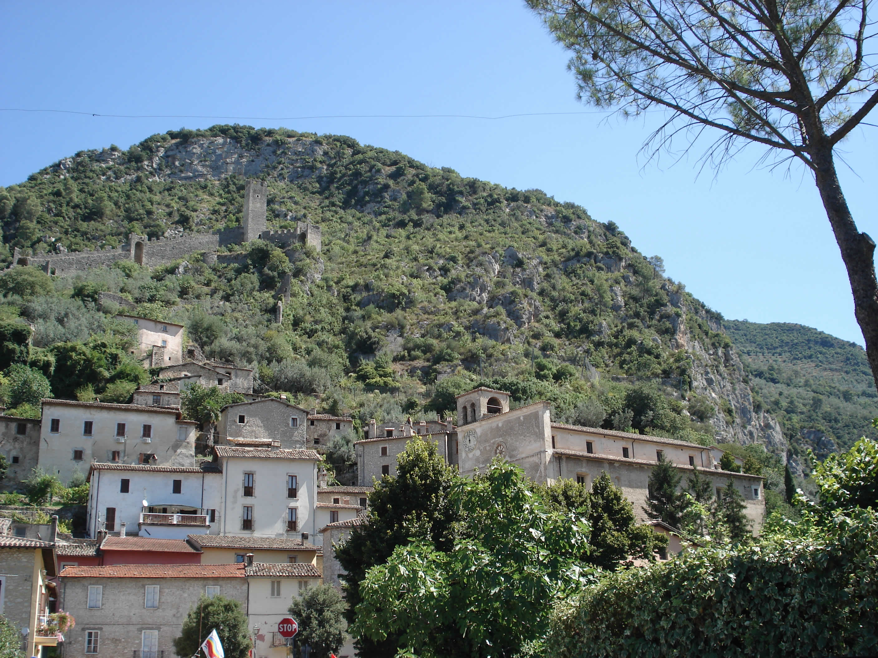Borgo di Ferentillo ai piedi della montagna, con case in pietra e le rovine del castello che dominano la valle.