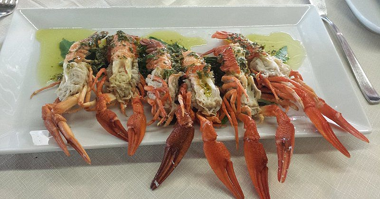 Prawns served on a bed of rocket with green sauce, plated on a white dish in an elegant restaurant.