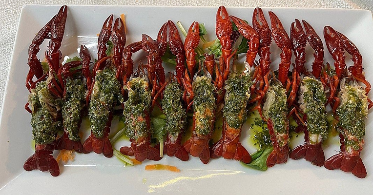 Prawns arranged in a row on a white dish, dressed with green sauce and served on a bed of rocket.
