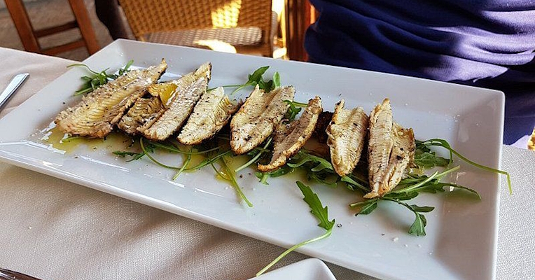 Grilled lake fish fillets (carbonaretti), served on a bed of rocket with extra virgin olive oil, plated on a white dish. (Photo credits: TRATTORIA TERESA)